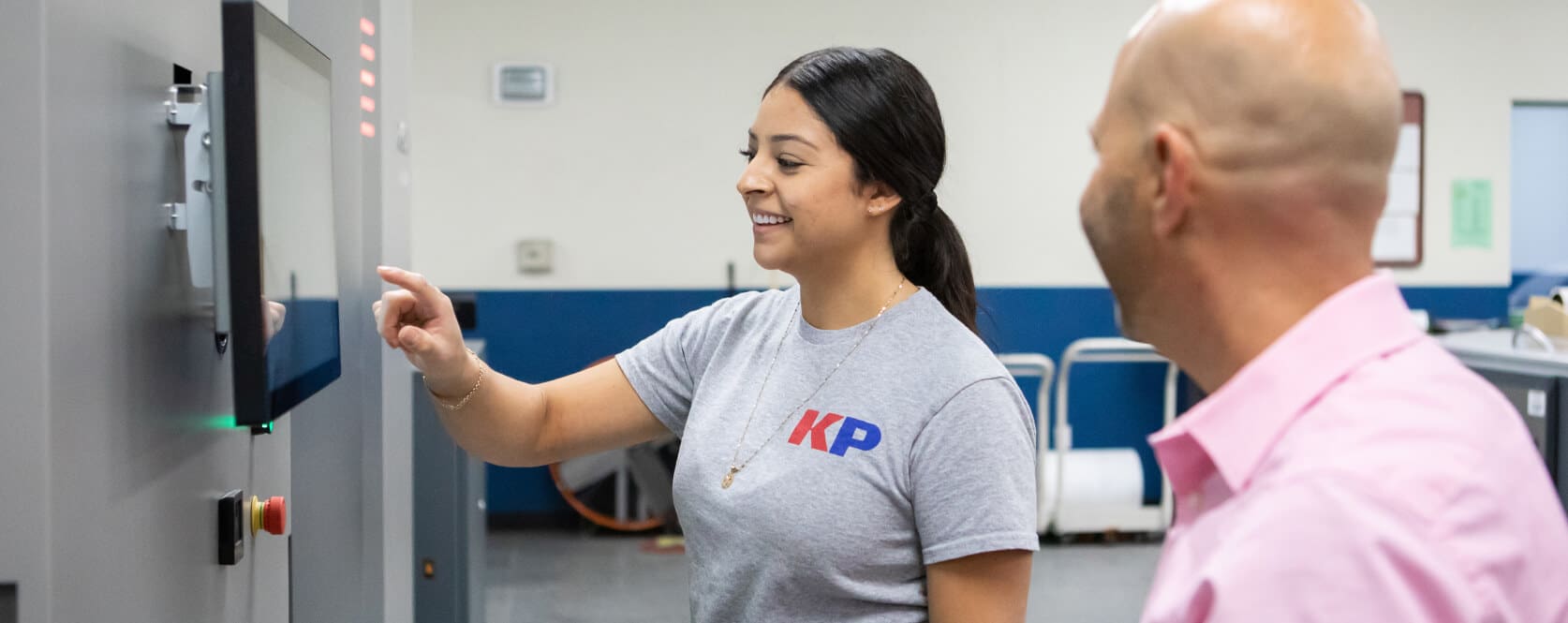 Smiling woman in KP shirt uses a wall mounted touch screen while talking to smiling man