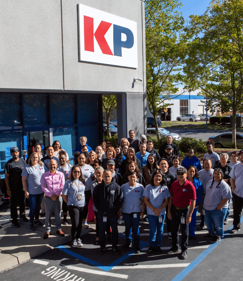 large group photo outdoors with 15+ employees posing outside of the KP Corp facility signage