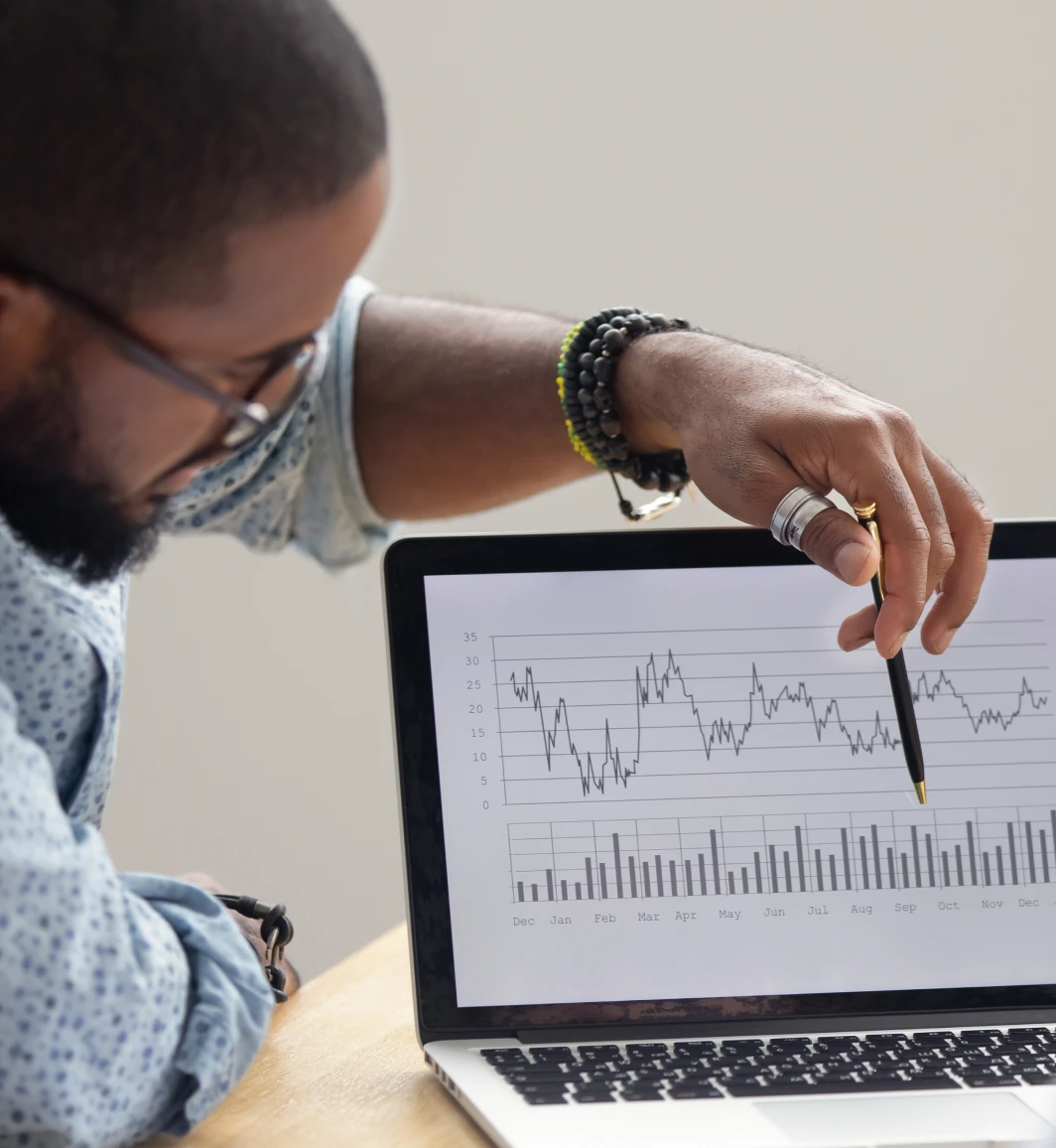 Man gesturing with his pen at a laptop screen showing a graph