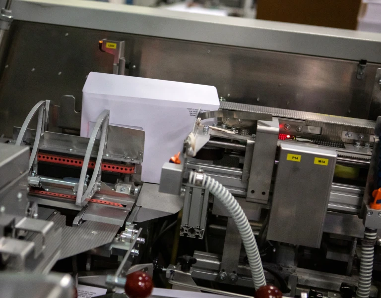 white envelope being printed on with black ink in a large silver machine during commercial printing process
