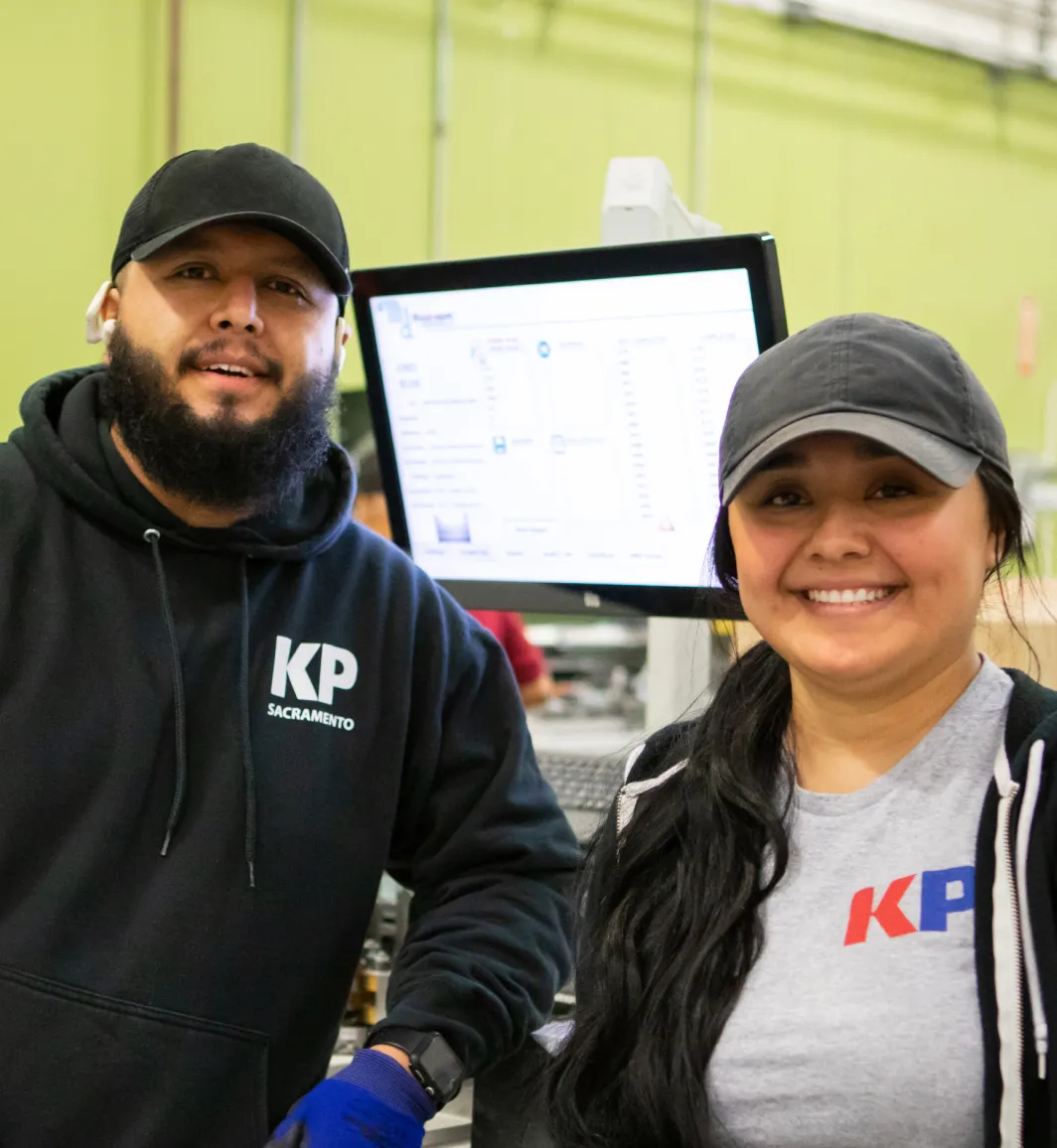 two KP Corp employees smiling one male in a black hat and one female in a gray hat
