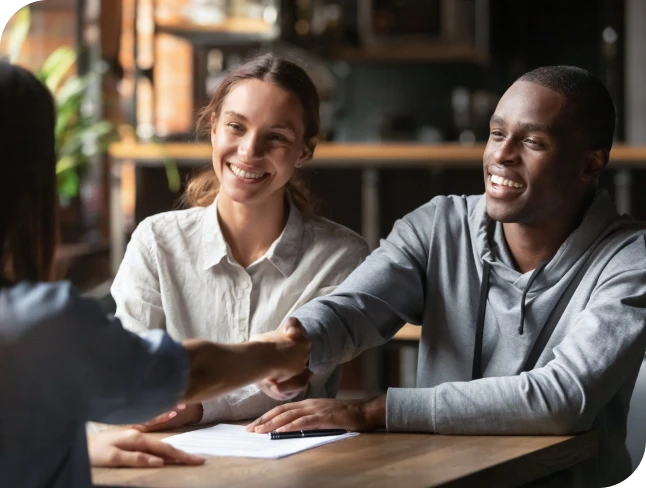 Man and woman smiling as the man shakes hands with another person across a desk