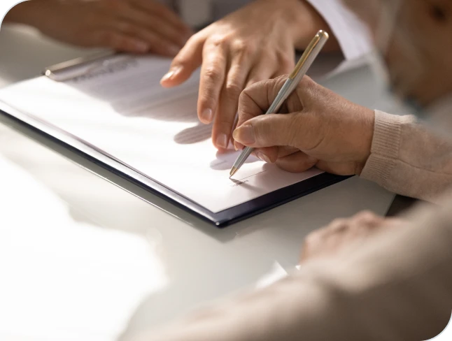 One person signing a form while another points to the page