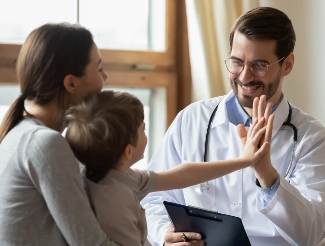 Mother holding her son as he gives a high five to a doctor