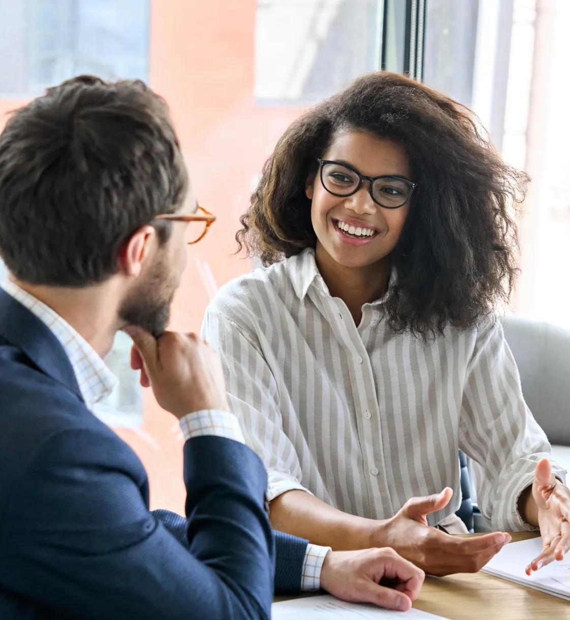 Black woman in glasses holding an ipad chatting with man in glasses at an office table