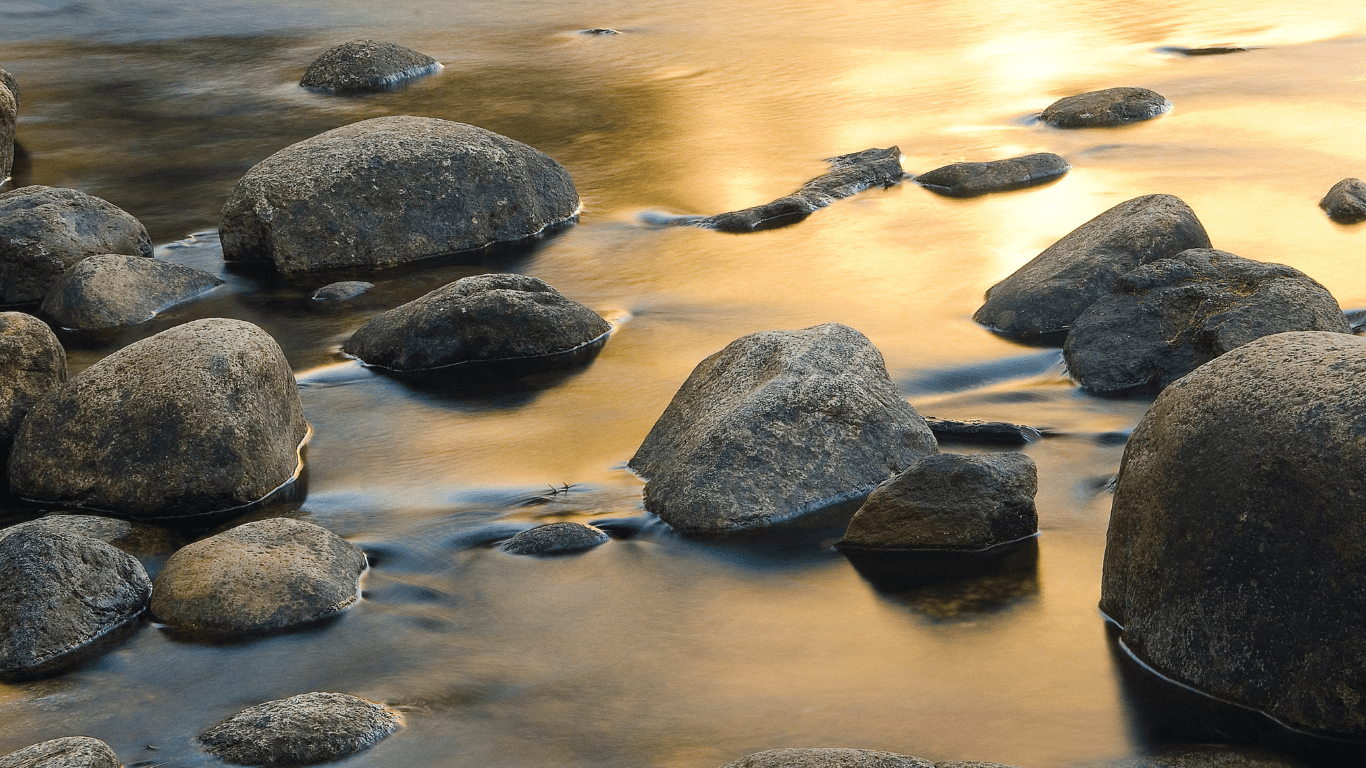Rocks in the river with sun shining on the moving water